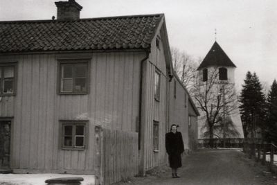 Kvinna stående bredvid ett hus på liten gata
Nyckelord: Hus Kyrktorn