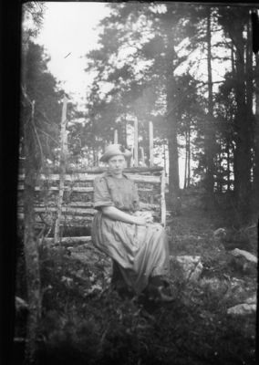 Kvinna sittande framför gärdesgård.
