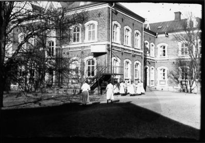 Kvinnor stående framför byggnad.
Nyckelord: Dräkt