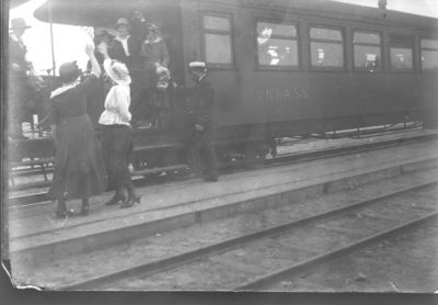 Män och kvinnor stående vid och på järnvägsvagn.
