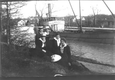 1 man och 4 kvinnor sittande vid vattendrag.
Nyckelord: Dräkt