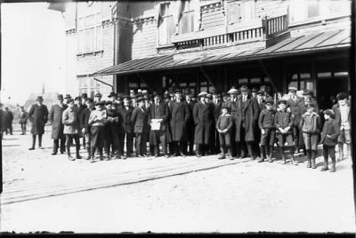 Ett antal personer stående framför byggnad.
