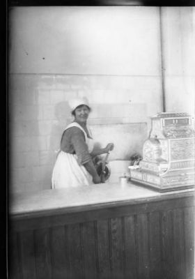 Kvinna stående bakom disken i affär.
Nyckelord: Kassa-apparat