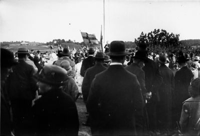 Ett antal personer stående vid flagga.
