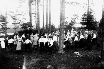 Ett antal personer dansande i skogsbacke.
Nyckelord: Dräkt
