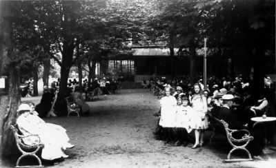 Ett antal personer sittande och stående i park.
Nyckelord: Parksoffa