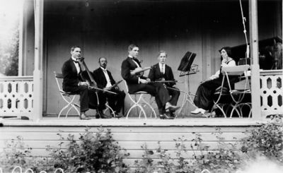 4 män och 1 kvinna sittande på musikestrad.
Nyckelord: Instrument Notställ