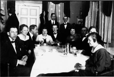 Ett antal personer sittande och stående runt ett kaffebord.
Nyckelord: Familjesammankomst