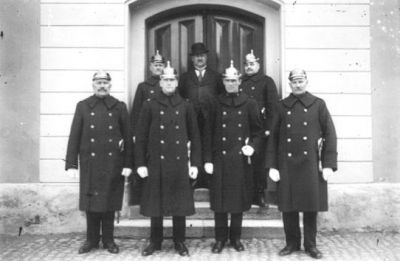 7 män stående utanför port.
Nyckelord: Uniform Polis