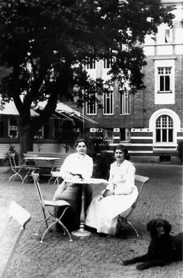 2 kvinnor sittande vid bord framför byggnad.
