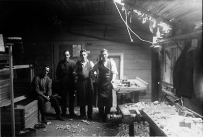 1 sittande och 3 stående män i en lokal.
Nyckelord: Hyvelbänk