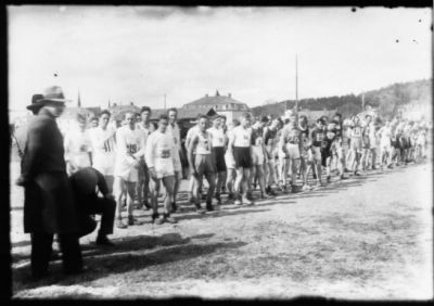 Ett antal idrottsklädda män stående på startlinje till löptävling.
Nyckelord: Löpning