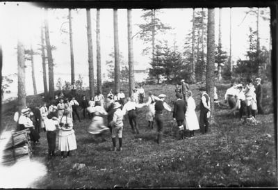 Ett antal personer dansande i skogsbacke.
Nyckelord: Skogsbacke Dräkt
