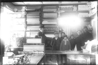 2 män, 1 kvinna och 4 barn stående bakom disken i affär.
Nyckelord: Affär Våg Omslagspapper