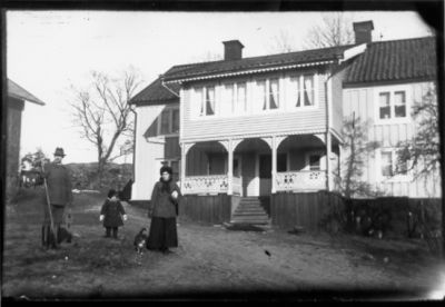 Man, kvinna och barn stående på gårdsplan.
Nyckelord: Katt Veranda