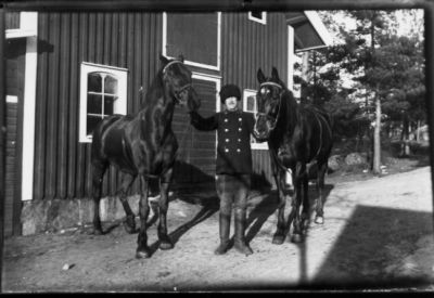 Man stående med 2 hästar framför byggnad.
Nyckelord: Häst