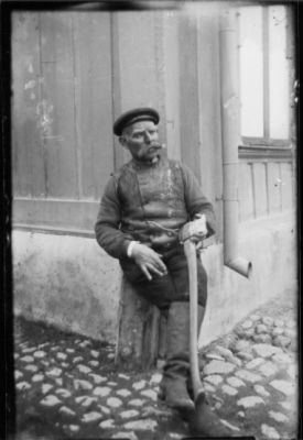 Man sittande mot husvägg.
Nyckelord: Käpp Kullersten Husknut