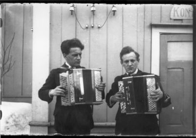 2 män stående och spelar dragspel på gård.
Nyckelord: Dragspel