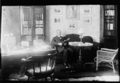 Man sittande vid bord.
Nyckelord: Bokhylla