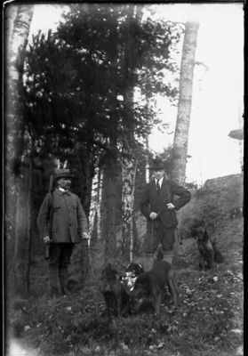 2 män stående i skogen med 2 hundar.
Nyckelord: Hund Gevär