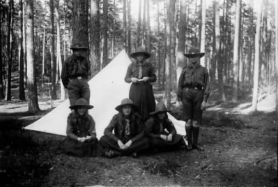 6 ungdomar i scoutuniform framför tält i skogsbacke.
Nyckelord: Tält