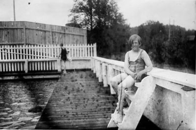 Flicka sittande på stege vid bad.
Nyckelord: Baddräkt