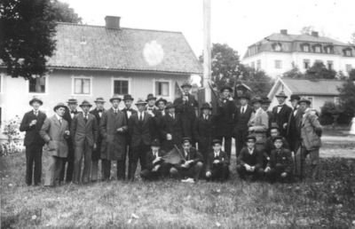 Ett antal män sittande och stående på gräsmatta.
Nyckelord: Flaggstång