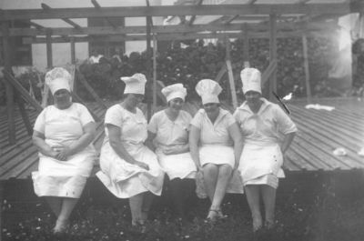 5 kvinnor sittande framför byggnad.
Nyckelord: Dräkt Kockmössa