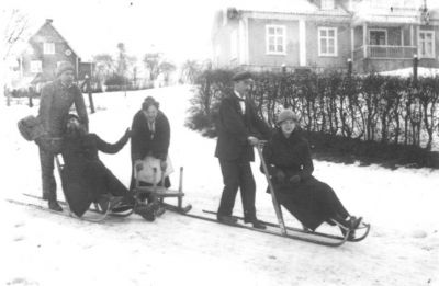 Man och kvinna sittande på spark, 2 män stående på spark och kvinna stående vid kälke.
Nyckelord: Spark Kälke Dräkt