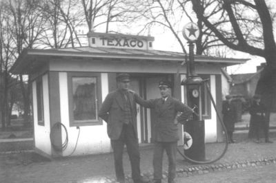 2 män stående vid bensinstation.
Nyckelord: Bensinpump Skärmmössa