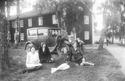 Man sittande på bil och 4 kvinnor sittande framför.
Nyckelord: Bil