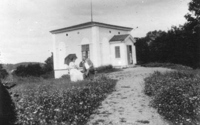 Man och kvinna sittande framför byggnad.
Nyckelord: Paraply Bänk