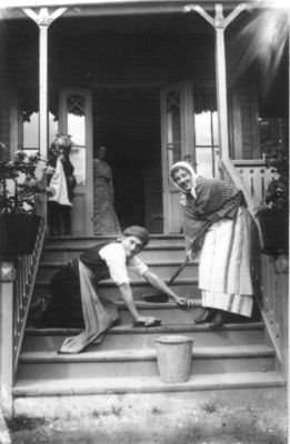 Man, på knä och kvinna, stående, tvättande trappa till byggnad.
Nyckelord: Hink Trappa Sopborste