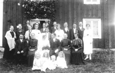 Ett antal personer på ett bröllopsfoto framför byggnad.
