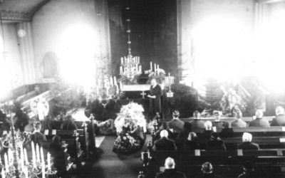 Ett antal personer sittande i kyrka vid begravning.
Nyckelord: Kista Ljuskronor