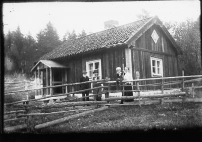 2 män och 1 kvinna stående bakom staket och ett barn sittande på staket.
Nyckelord: Staket