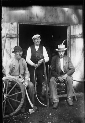 3 män. En sittande med yxa, en stående med såg och en sittande på pall.
Nyckelord: Såg Yxa Uthus