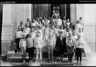 Kvinna och ett antal barn stående på skoltrappa.
Nyckelord: Skolklass