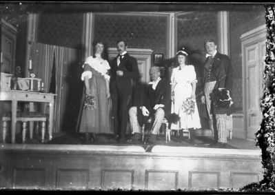 2 stående män, 2 stående kvinnor och 1 sittande man på scen.
Nyckelord: Lokal Teater