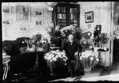 Man sittande bland blommor i ett rum.
Nyckelord: Interiör Blommor