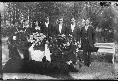 4 män och 3 kvinnor stående bakom kista.
Nyckelord: Kista Krans