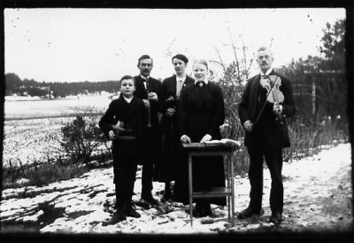 2 män, 2 kvinnor och en pojke stående vid en cittra.
Nyckelord: Cittra Fiol Vinter