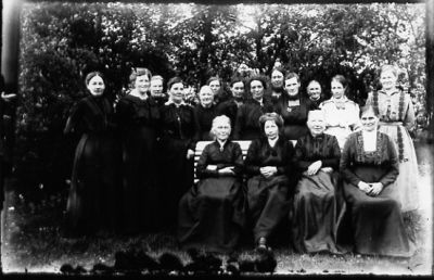 Ett antal kvinnor stående bredvid och 4 sittande på parkbänk.
Nyckelord: Park Växtlighet