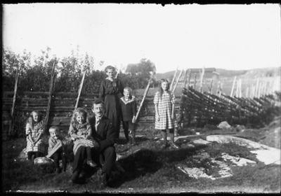 Familj sittande och stående i hage.
Nyckelord: Gärdesgård Natur