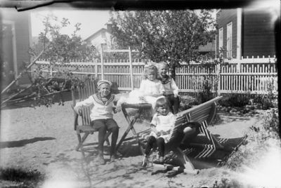 2 pojkar och 2 flickor sittande i trädgårdsmöbel.
Nyckelord: Trädgårdsmöbel Staket