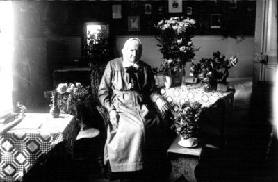 Kvinna sittande i rum bland blommor.
Nyckelord: Pall Blommor