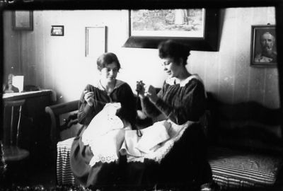 2 kvinnor sittande i soffa med broderier i knät.
Nyckelord: Soffa Tavla Broderi