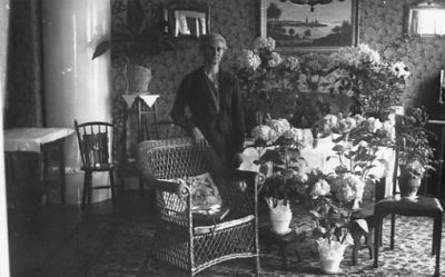 Kvinna stående vid bord med blommor.
Nyckelord: Födelsedag Blommor Kakelugn Tavla Pedistal
