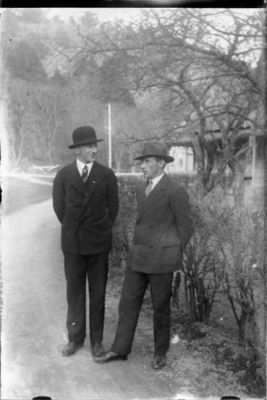 2  män stående på väg intill häck.
Nyckelord: Väg Häck