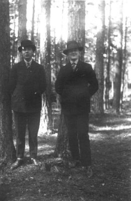 2 män stående i skogsbacke.
Nyckelord: Träd